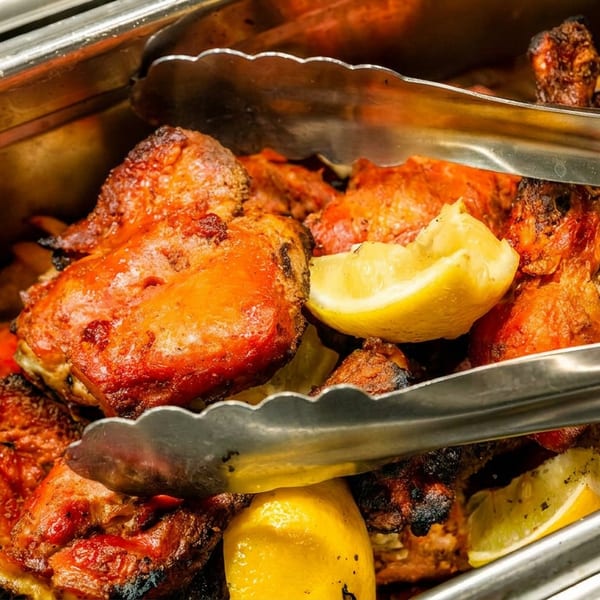 Tandoori chicken pieces with lemon wedges in a metal serving tray with tongs.