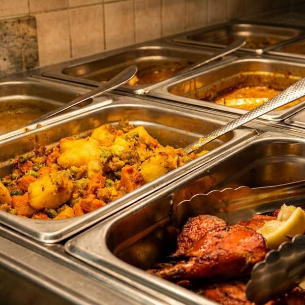 A buffet line with various Indian dishes in metal warming trays, including chicken and vegetables.