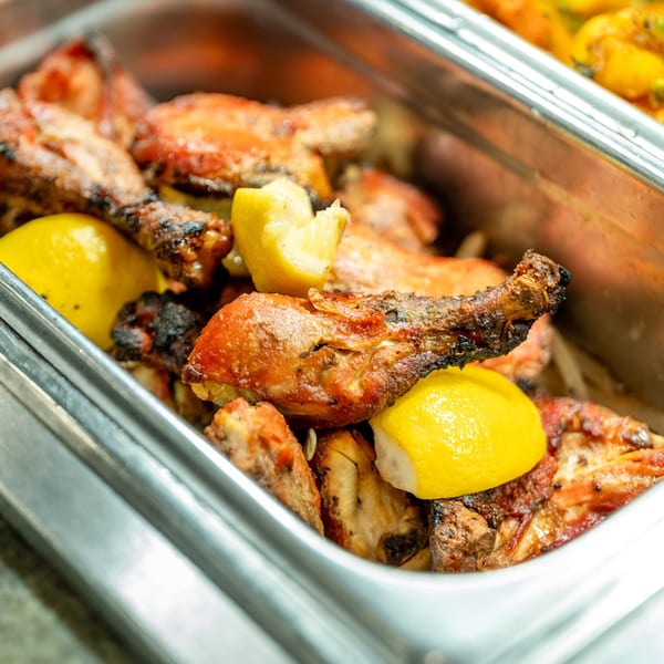 Grilled chicken drumsticks and wings with lemon wedges in a metal serving tray.