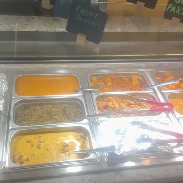 A buffet line with various Indian dishes like Paneer Korma, Mixed Veg, and Kadhi Pakora.