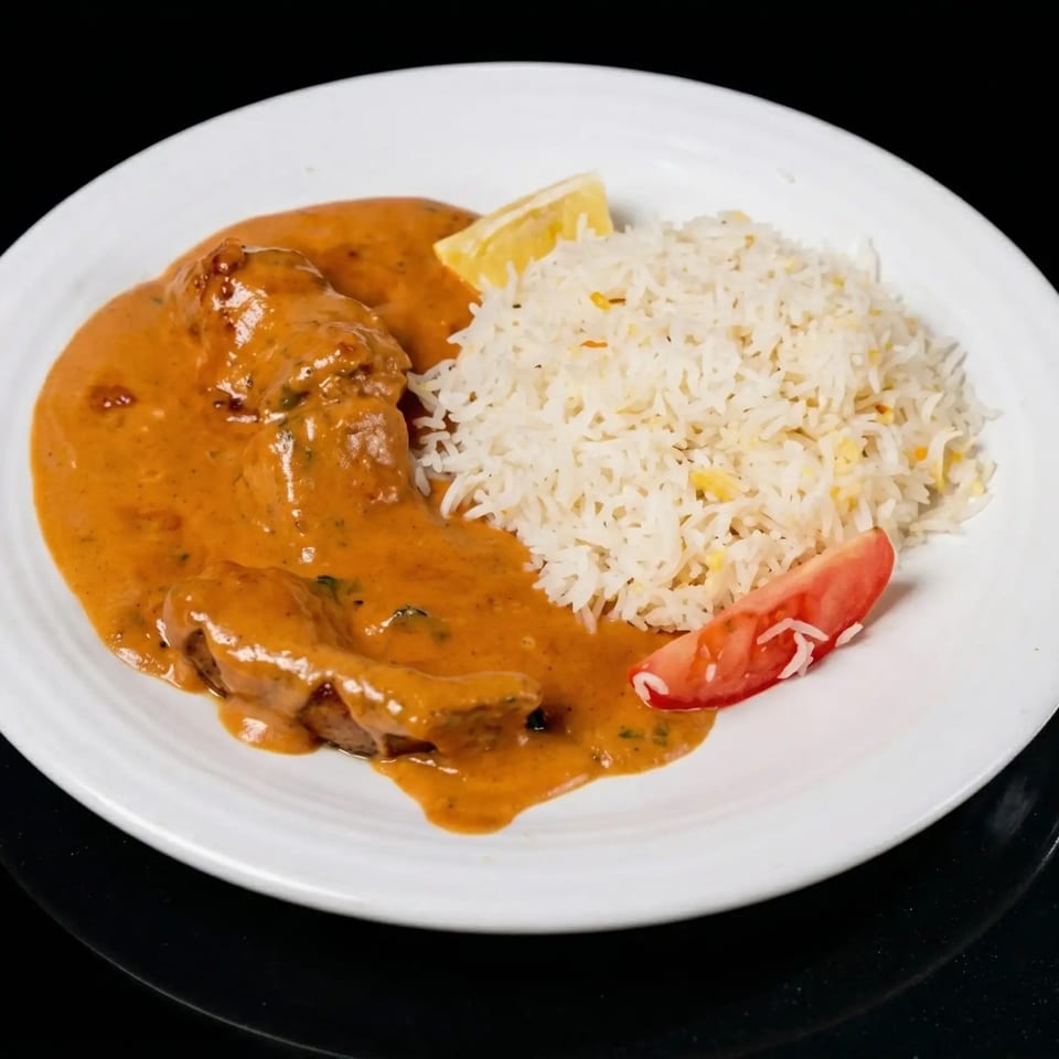 Chicken curry with rice, a lemon wedge, and a tomato slice on a white plate.