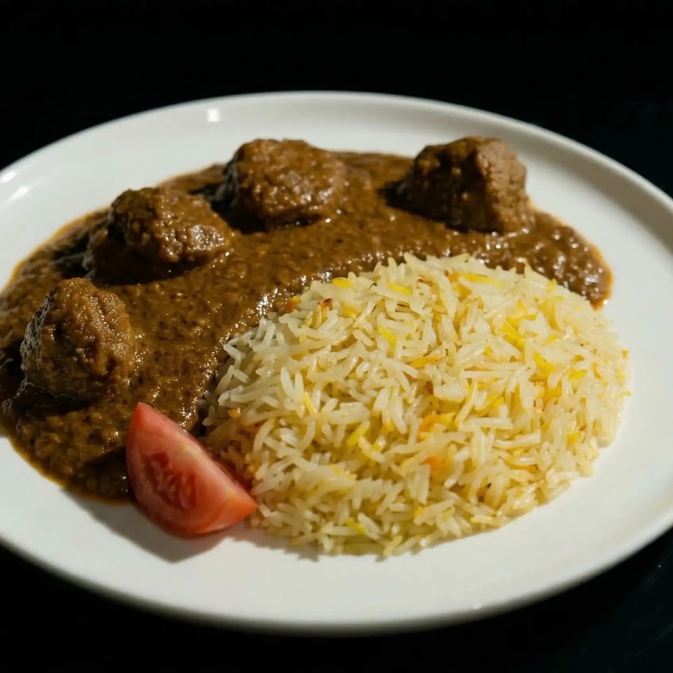 Meatballs in a rich brown sauce with a side of rice and a tomato wedge.