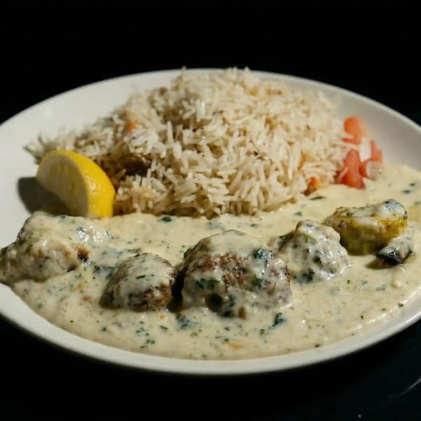 Creamy chicken dish with rice, a lemon wedge, and diced tomatoes on a white plate.