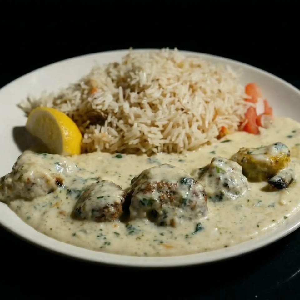 Creamy chicken dish with rice, a lemon wedge, and diced tomatoes on a white plate.
